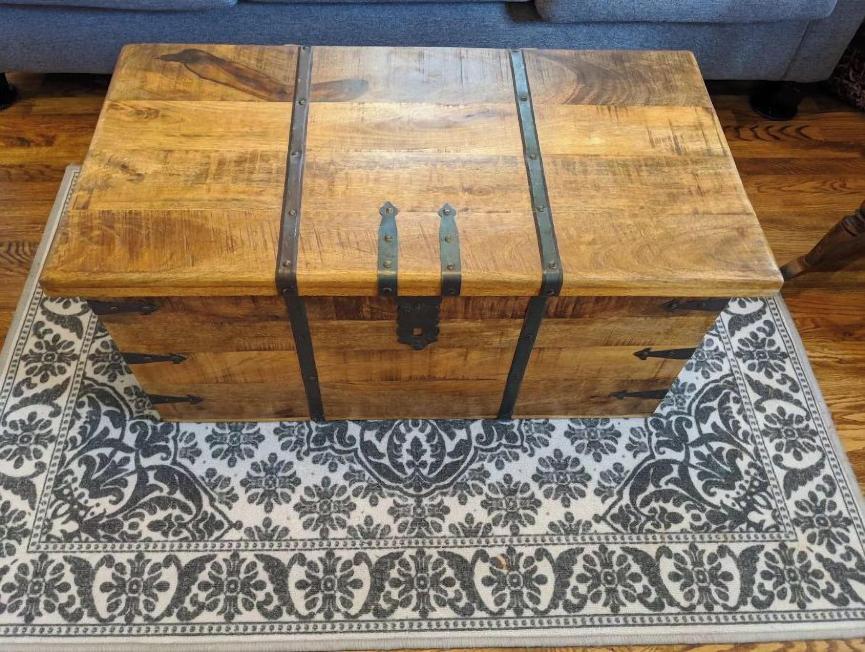 A wooden chest with metal straps on a patterned rug.