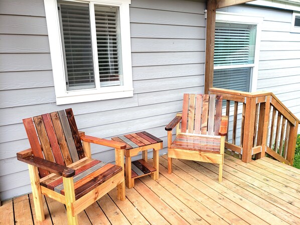 A wooden deck with two Adirondack chairs and a small table.