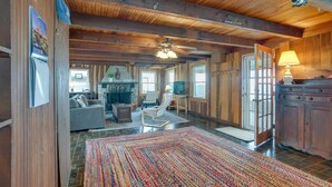 A spacious living area with a large rug, wooden ceiling beams, a ceiling fan, and a television. - Historic Cottage w/ Beautiful Oceanfront View (Marshfield)