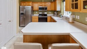 Una cucina con mobili in legno, un frigorifero in acciaio inossidabile, un forno a microonde e un piano cottura. C'è un ripiano bianco e una piccola isola con due sedie.