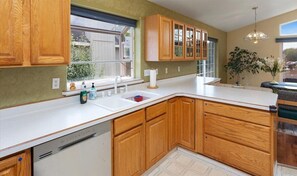 Une cuisine avec des meubles en bois, un plan de travail blanc, un lave-vaisselle encastré et une fenêtre donnant sur l’extérieur.