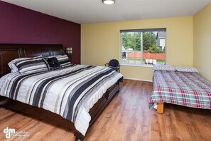 Une chambre à coucher avec un grand lit, un plus petit lit, une chaise et une fenêtre donnant sur l’extérieur.