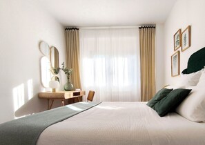 Une chambre d’hôtel avec un lit, un bureau, une chaise, un miroir et des rideaux.
