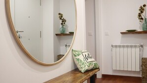 Une pièce comprenant un banc en bois, un grand miroir, un radiateur et une étagère ornée d’objets décoratifs.