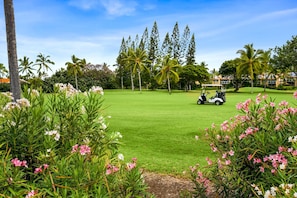 A golf course with a golf cart, palm trees, and flowering plants.