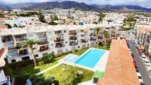 A residential area with a swimming pool surrounded by apartment buildings, a road, and mountains in the background. - AP368 - Coronado 67 (Nerja)