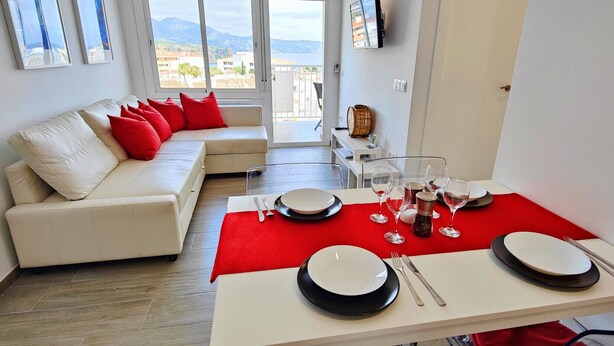 A modern living room with a sofa, red cushions, a dining table set with plates, glasses, and cutlery. - AP368 - Coronado 67 (Nerja)