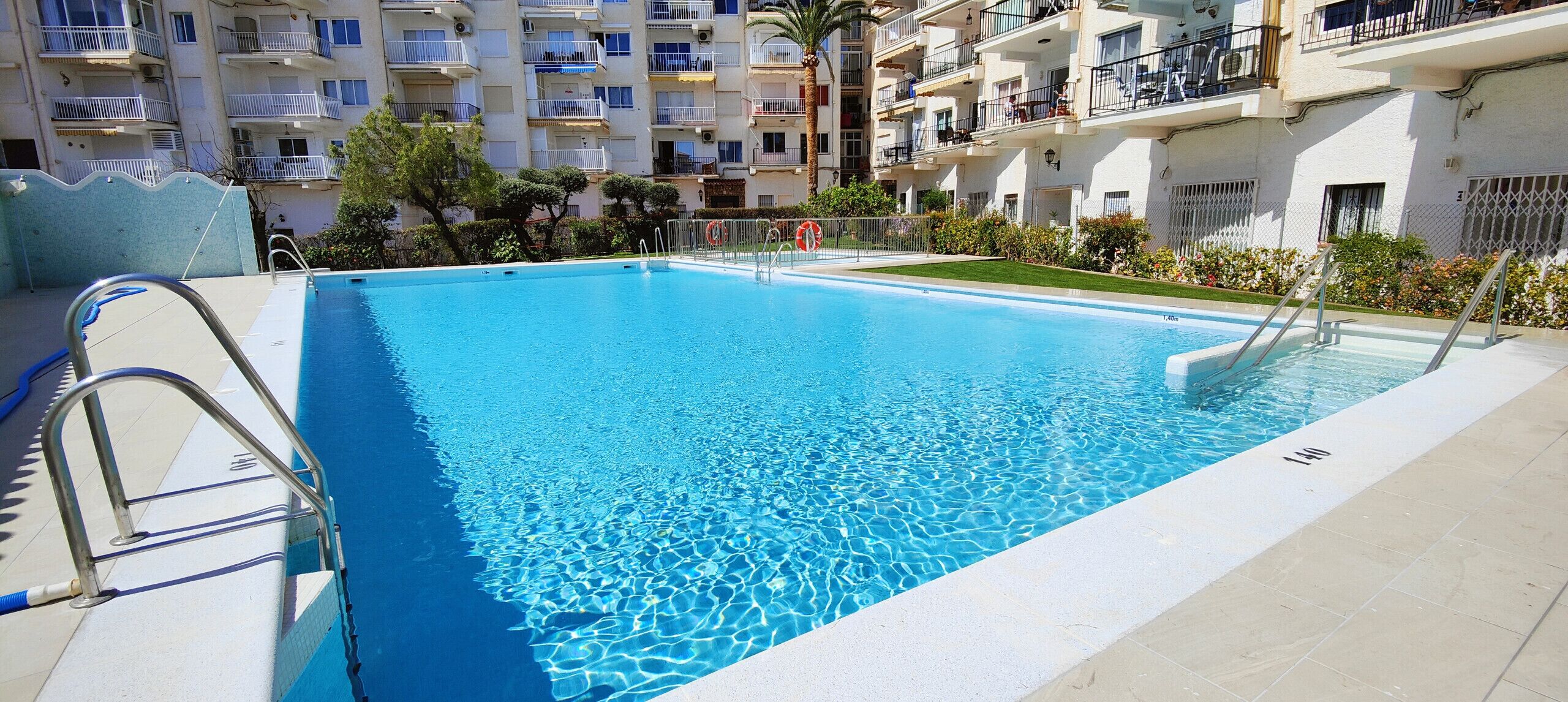 Une piscine rectangulaire à l’eau d’un bleu limpide, entourée d’une terrasse carrelée et de rampes métalliques au bord du bassin.