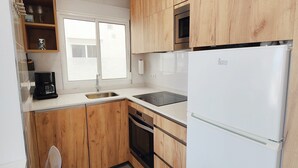 A kitchen with wooden cabinets, a white refrigerator, a coffee maker, and a window. - AP368 - Coronado 67 (Nerja)