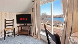 Une pièce avec une grande fenêtre, un téléviseur, une chaise et une table.