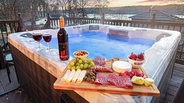 Un bain à remous avec une terrasse en bois et une table où sont disposés de la nourriture et des boissons.