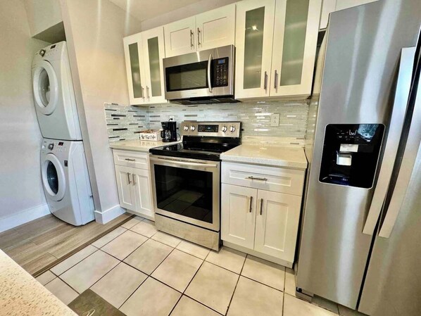 A modern kitchen with stainless steel appliances, including a microwave, oven, and refrigerator. There is a washing machine to the left. - Quiet retreat near Coconut Grove + free parking (Miami)
