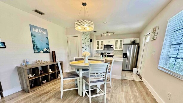 A modern kitchen with white cabinets, stainless steel appliances, and a dining area with a round table and chairs. - Quiet retreat near Coconut Grove + free parking (Miami)