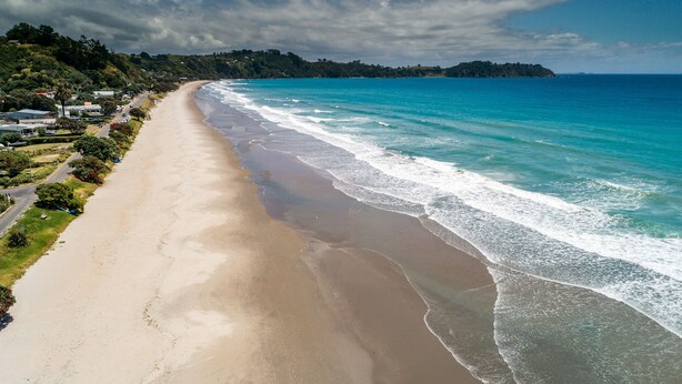 A long, sandy beach with gentle waves, a clear sky, and a distant island. - All day sun house with metres away from the golden sands of Onetangi Beach. (Waiheke Island)