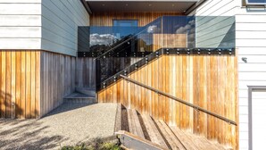 A modern house with a wooden exterior, a glass balcony, and a metal staircase. - All day sun house with metres away from the golden sands of Onetangi Beach. (Waiheke Island)
