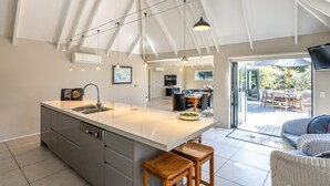 A modern kitchen with a central island, stainless steel appliances, and pendant lighting. - All day sun house with metres away from the golden sands of Onetangi Beach. (Waiheke Island)