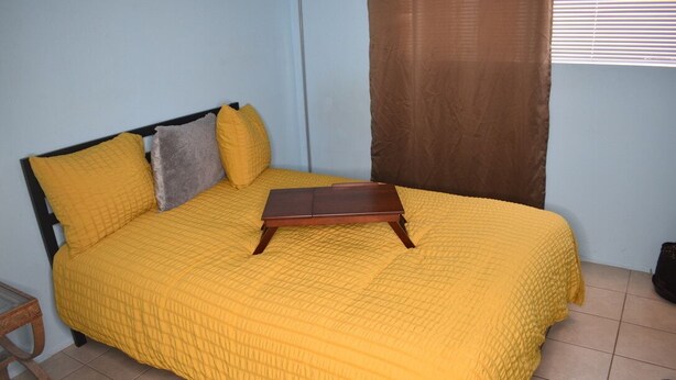A bed with a yellow quilt, a wooden bedside table, and a brown curtain. - Wake & Bake Vegas (Las Vegas)