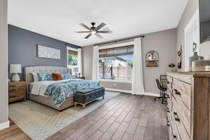 A bedroom with a bed, a nightstand, a dresser, a ceiling fan, and a window with curtains.