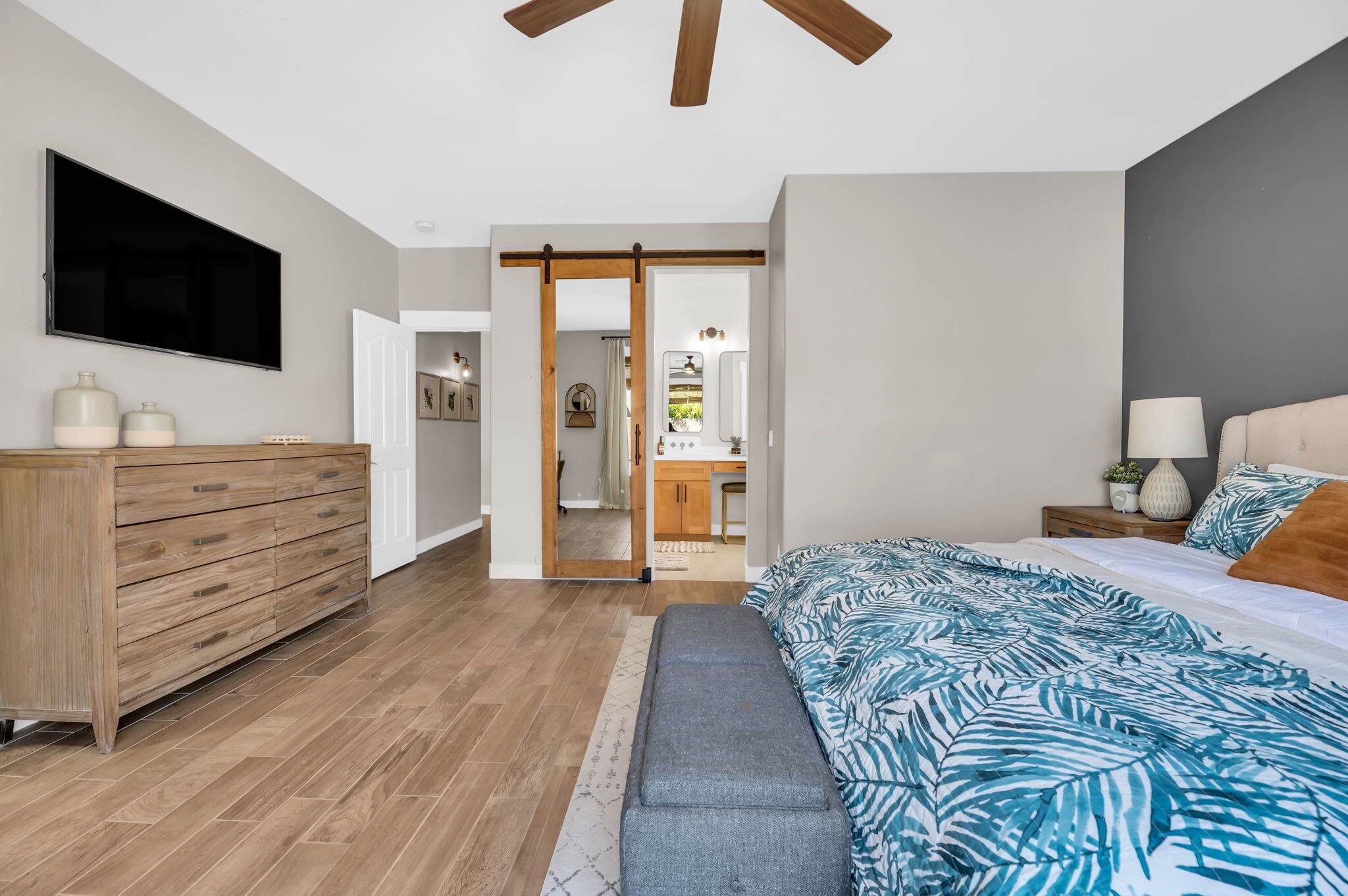 A bedroom with a bed, a dresser, a TV, and a sliding door leading to a bathroom.