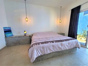 Une chambre moderne avec un grand lit, deux tables de chevet, une commode, un tableau et une vue sur l’extérieur.