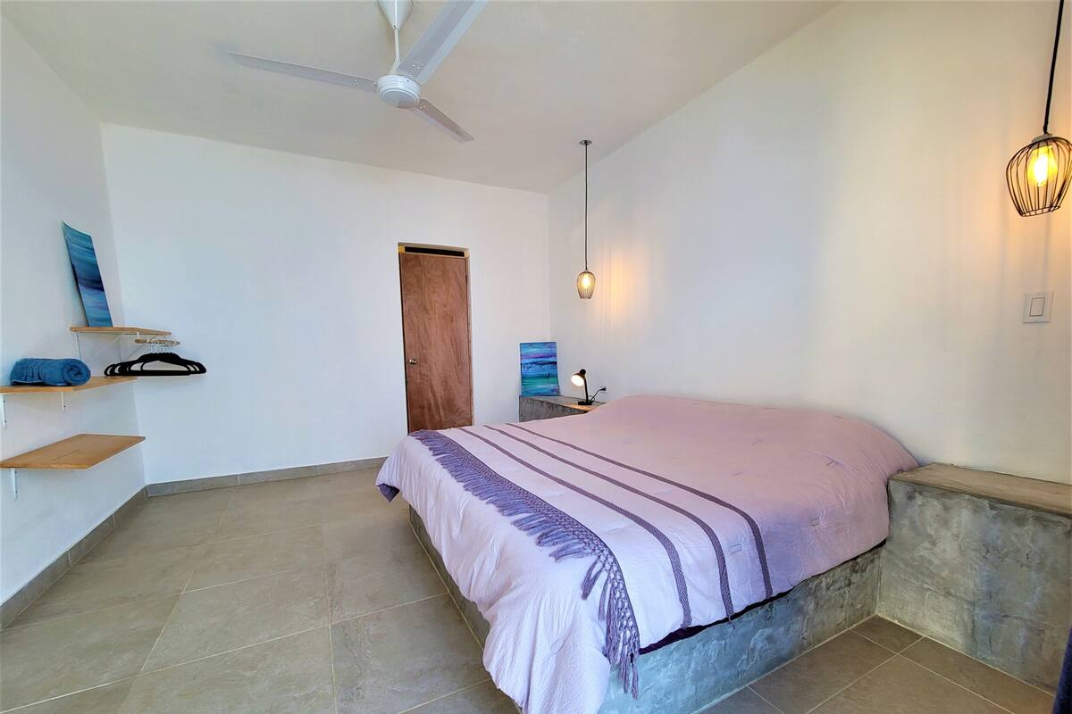 Une chambre à coucher avec un lit, un ventilateur de plafond, une lampe fixée au mur et une porte.