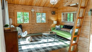 A cozy cabin interior with a checkered floor, wooden walls, a green sofa, a small round table, and a ladder.