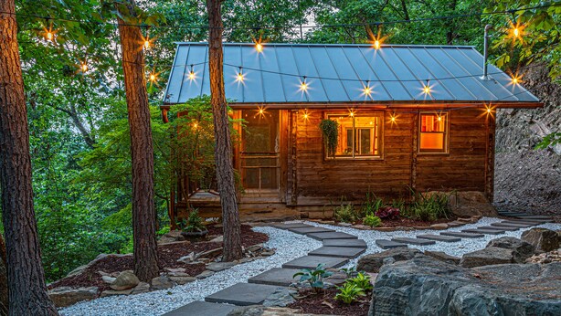 A rustic cabin with a metal roof, surrounded by trees and a stone pathway.