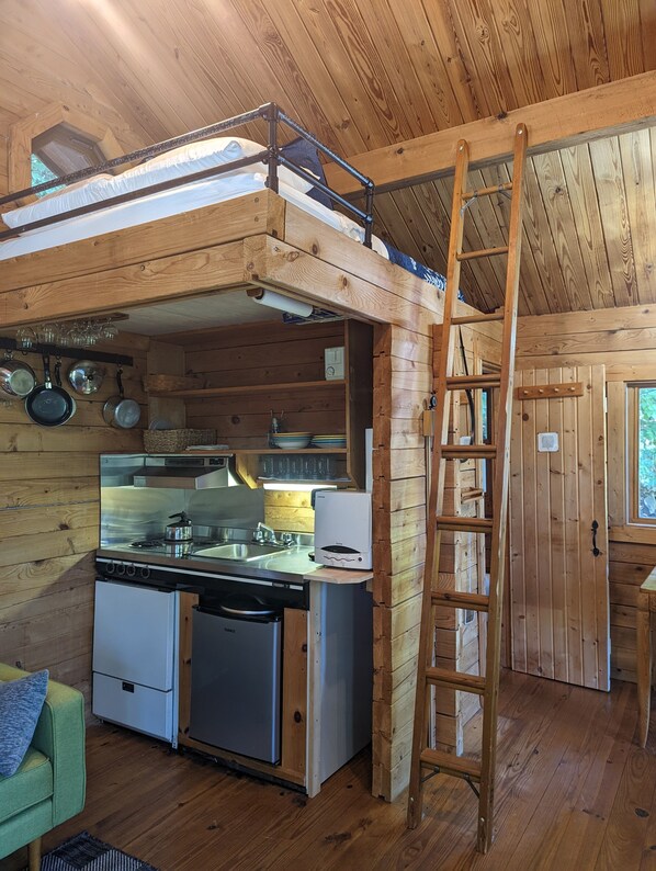 A compact kitchen with a built-in stove, sink, and dishwasher, wooden walls, and a lofted sleeping area.