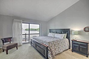 Ein Schlafzimmer mit einem großen Bett, einer Bank, einem Nachttisch und Blick auf ein Gewässer durch ein Fenster.
