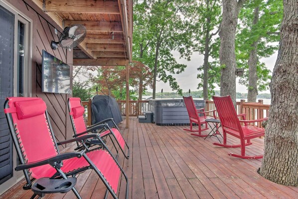 Eine Holzterrasse mit roten Stühlen und Grillplatz, mit Blick auf ein Gewässer.