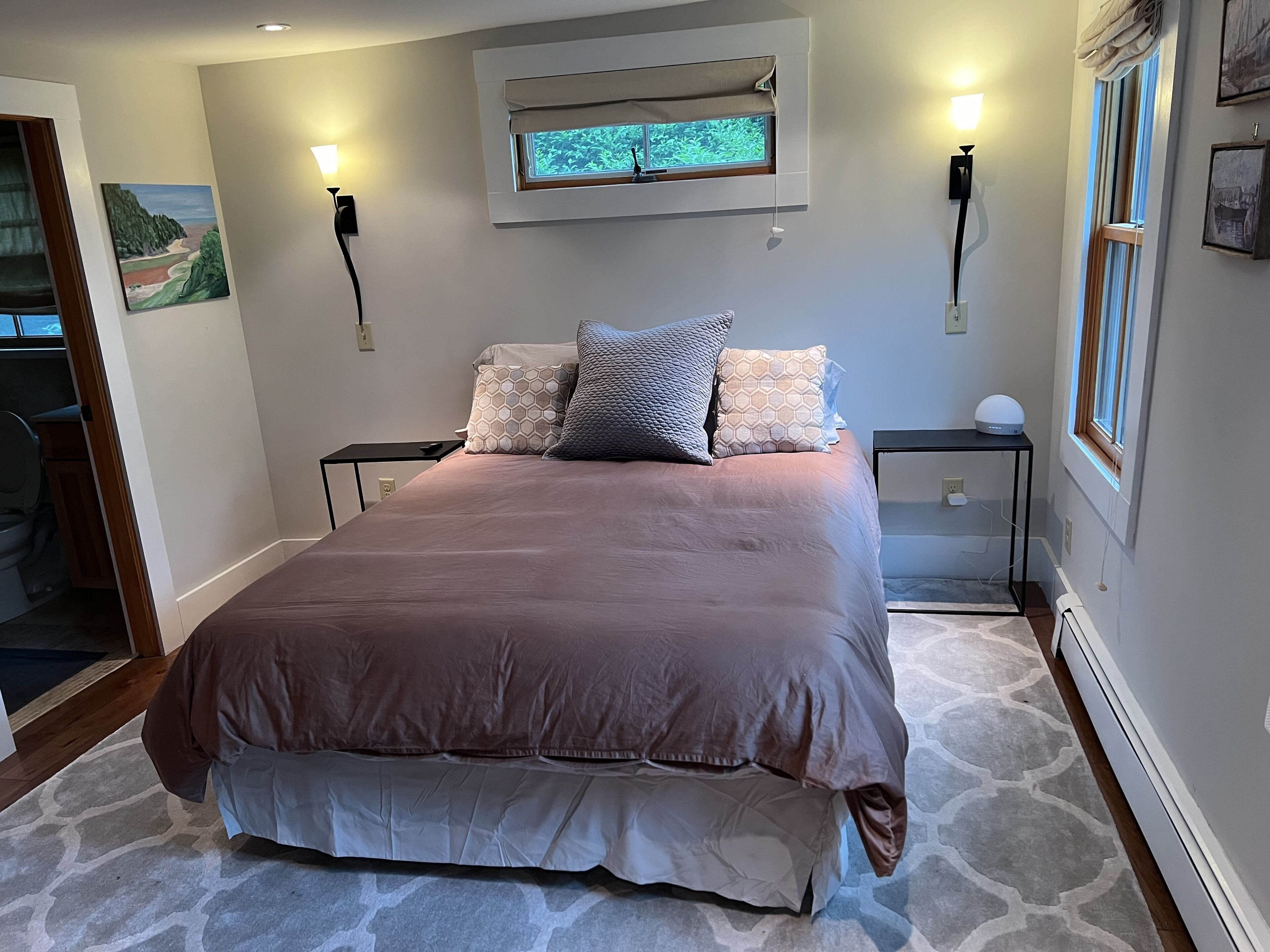 A bedroom with a large bed, two bedside tables, a window with a view, and a painting on the wall.