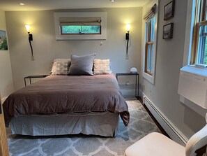 Une chambre avec un grand lit, deux tables de chevet, une fenêtre donnant sur un beau paysage et un climatiseur fixé au mur.