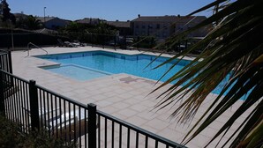 Ein rechteckiger Swimmingpool mit einer gefliesten Liegefläche, umgeben von einem schwarzen Metallzaun.