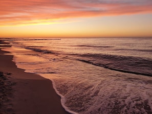 A beach with waves at sunset, a wooden pier, and a clear sky.