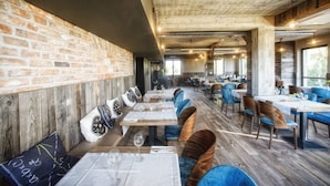 A restaurant with brick walls, wooden floors, and blue upholstered chairs. Tables are set with white tablecloths and wine glasses. - Residence Szary (Michalowice)