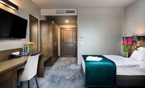 Una habitación de hotel con cama, escritorio, silla, televisor y armario.