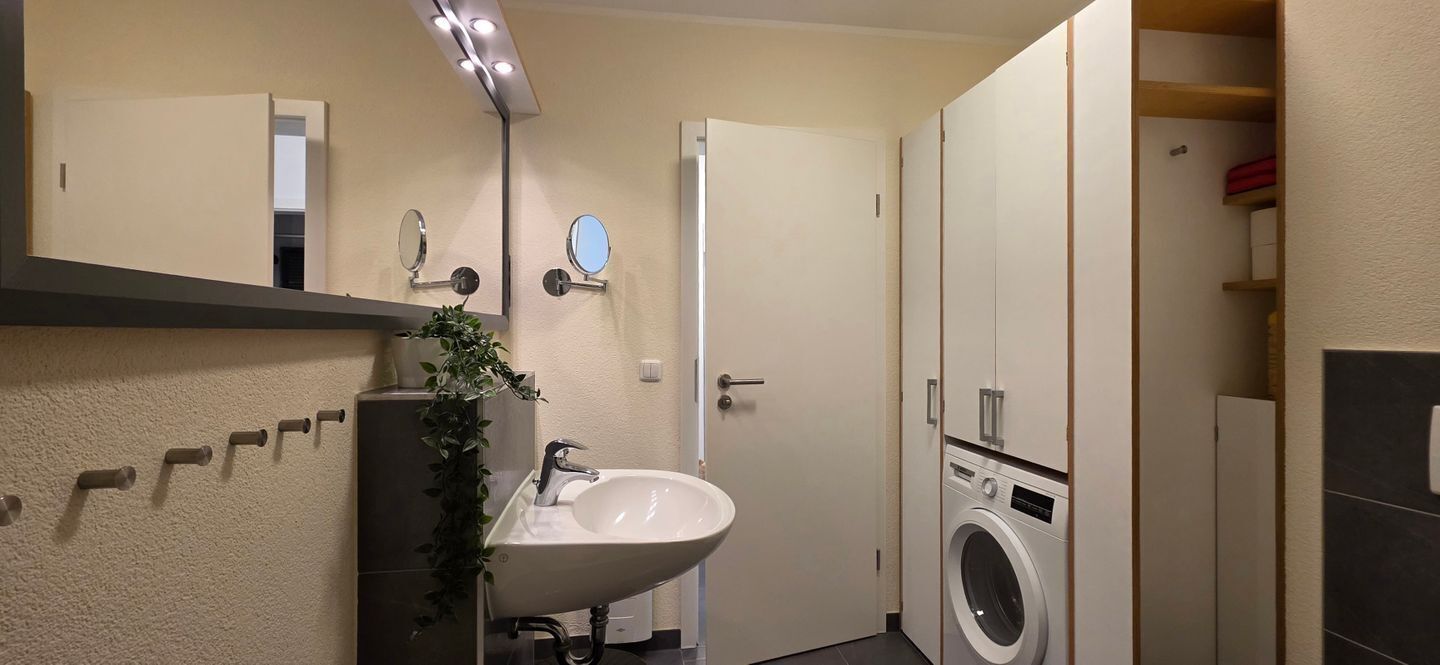 Ein kleines Badezimmer mit Waschbecken, Spiegel und Waschmaschine.