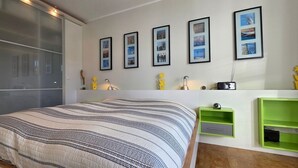 Un dormitorio moderno con una cama grande, una puerta corrediza de vidrio y una pared con fotos enmarcadas y estanterías verdes.