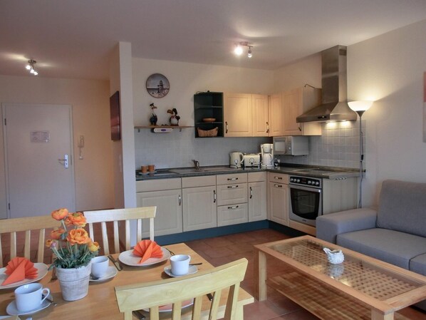A compact kitchen with a stove, microwave, and cabinets. There's a dining table with chairs and a small coffee table.