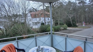 A balcony with two chairs and a small table, overlooking a residential area with houses and trees.