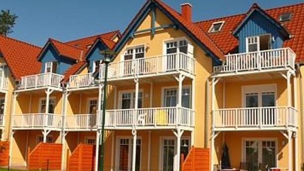 A row of yellow buildings with red roofs and white balconies. - Apartment K5 - 3-room apartment for 5 people. on the 2nd floor (Graal-Müritz)