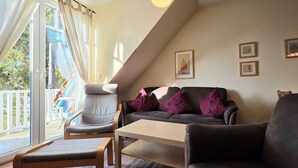 A living room with a sofa, armchair, and table, a balcony with curtains, and framed pictures on the wall. - Apartment K5 - 3-room apartment for 5 people. on the 2nd floor (Graal-Müritz)