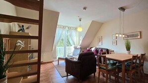 A dining area with a wooden table and chairs, a sofa, and a balcony with a view. - Apartment K5 - 3-room apartment for 5 people. on the 2nd floor (Graal-Müritz)