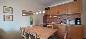 A compact kitchen with wooden cabinets, a microwave, a stove, and a coffee maker. There is a dining table with chairs and a potted plant.