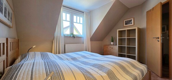 A bedroom with a bed, a window, a radiator, a wooden cabinet, and a door.