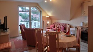 Comedor con una mesa lista para cuatro, sillas, lámpara en el techo y vista al exterior por una puerta corrediza de vidrio.