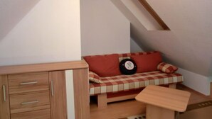 Una habitación pequeña y acogedora con techo inclinado, un banco de madera con cojín a cuadros y una mesita.