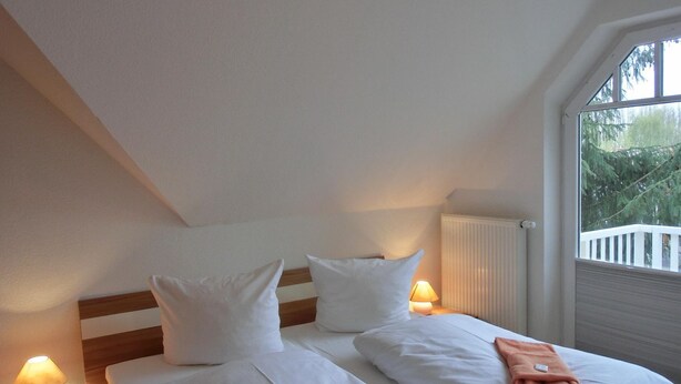 Habitación doble con dos camas, cada una con ropa blanca de cama y almohadas, una mesita de noche con lámpara y vistas a árboles a través de una ventana.