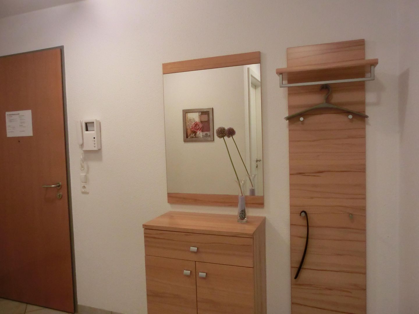 Ein Zimmer mit einem Holzschrank, einem Spiegel, einer kleinen Kommode mit Blumen und einer Tür mit einem Schild.