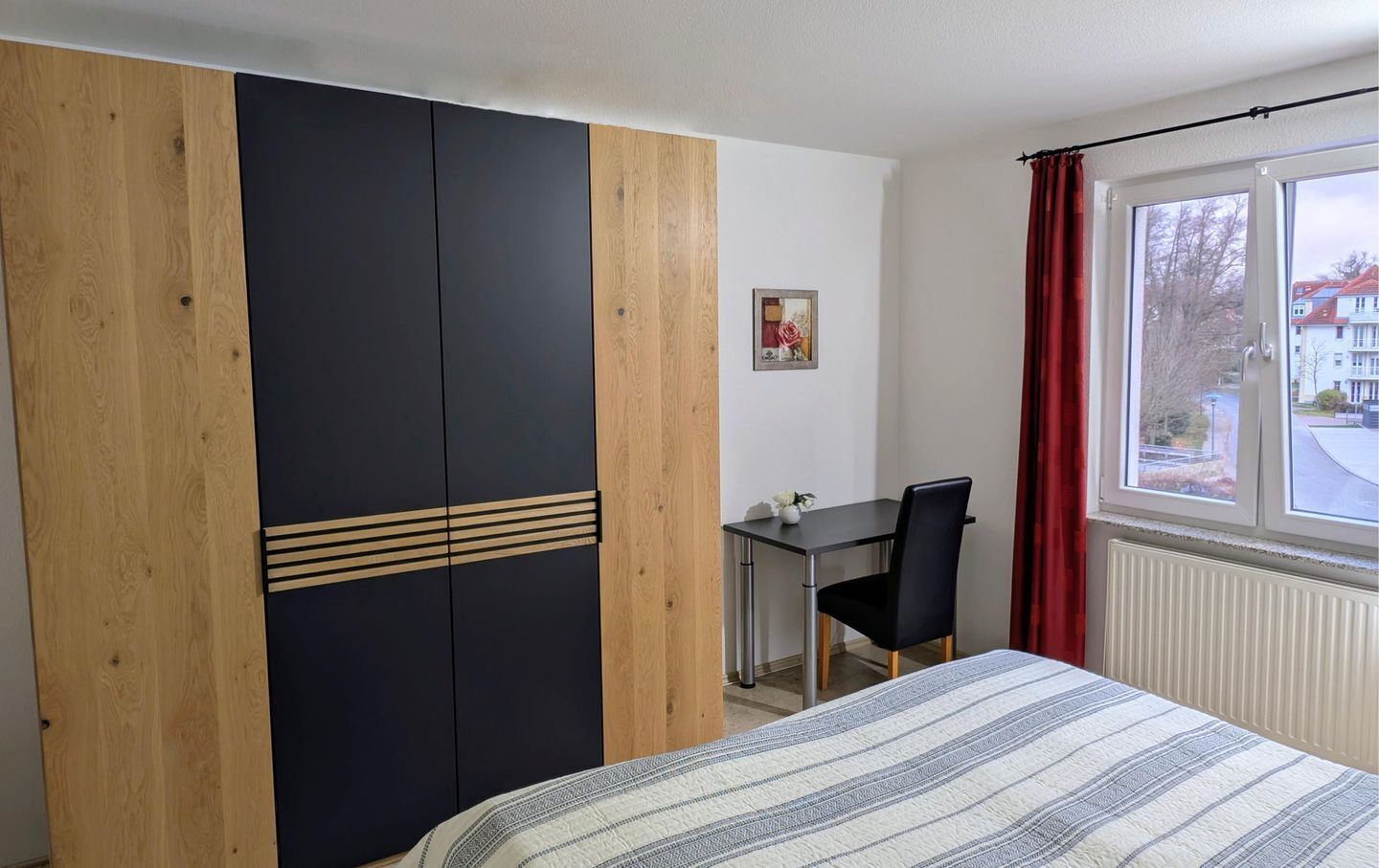 Ein Schlafzimmer mit Bett, Schreibtisch und Stuhl. Ein Fenster mit Vorhängen.